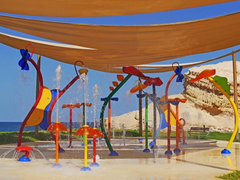 Colorful water playground with shade canopy and rocks in the background at the beach.