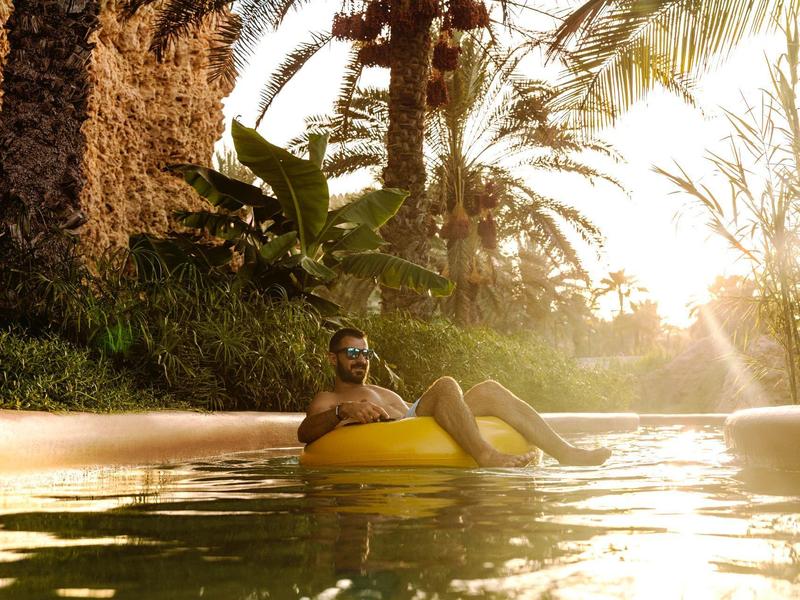 Man relaxing on a yellow pool float in the pool at sunset