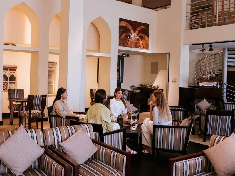 Guests sit in an elegant hotel lounge with tall arched windows and wooden paneling.