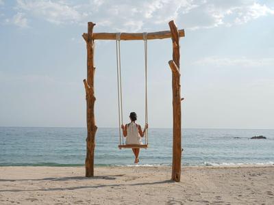 Person auf Schaukel am Strand mit Blick auf das Meer bei klarem Himmel.
