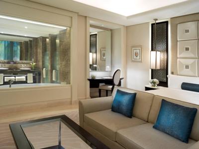 Habitación de hotel moderna con sofá, pared de vidrio hacia el baño y decoración elegante.