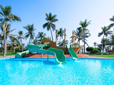 Ein Pool mit Wasserrutschen und Palmen im Hintergrund unter klarem blauem Himmel.