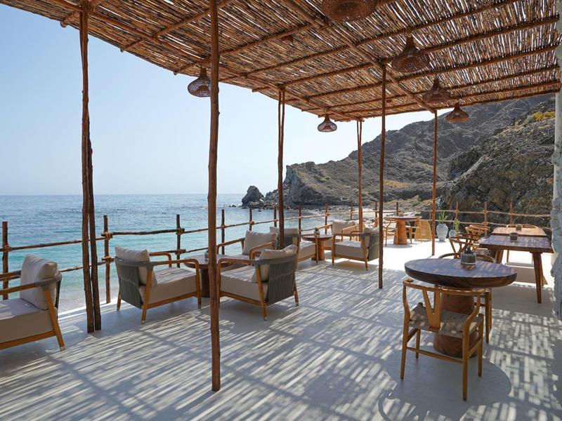 Terraza cubierta con sillas y mesas con vista al mar en un día soleado.