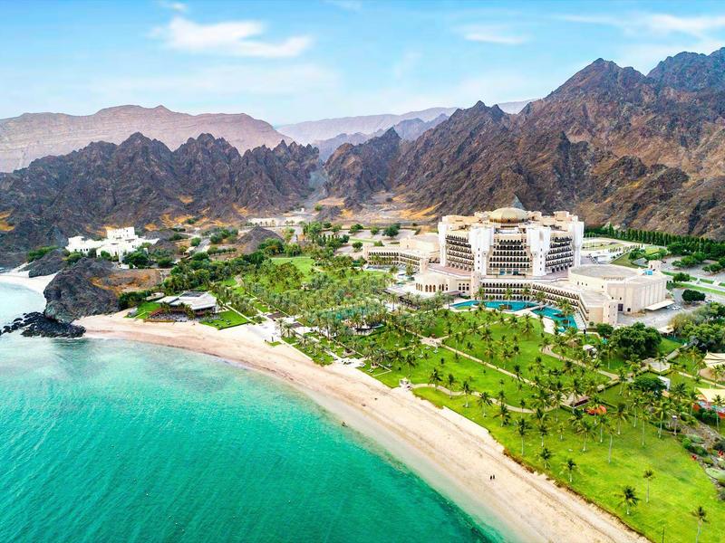 Resort de lujo con playa y montañas al fondo, rodeado de áreas verdes.
