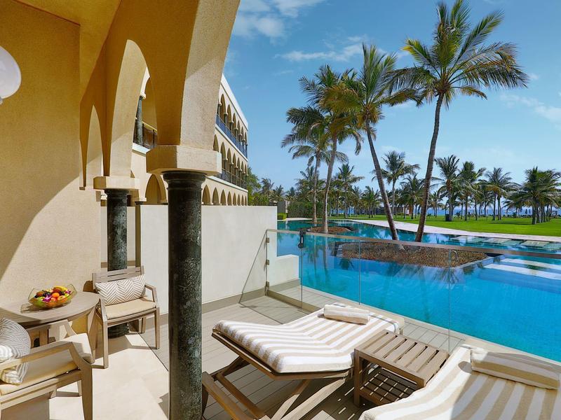 Terraza soleada del hotel con piscina, tumbonas y vistas a palmeras y cielo azul.