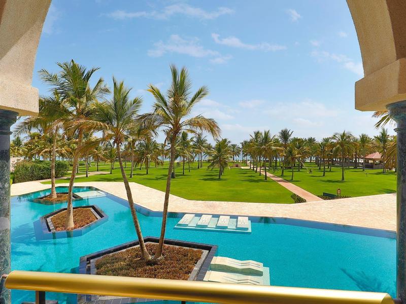 Vista a través de un arco de una piscina tropical con palmeras y tumbonas en un resort.