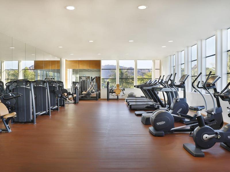 Gimnasio luminoso con equipamiento moderno y grandes ventanas con vista a zonas verdes.