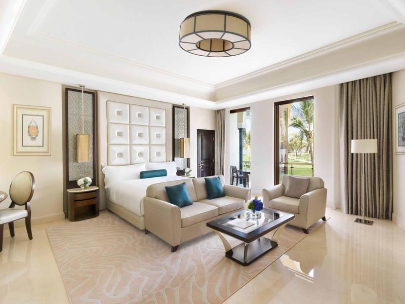 Sala de estar amplia y luminosa con sofá beige, sillas, mesa de café y grandes ventanas con cortinas.