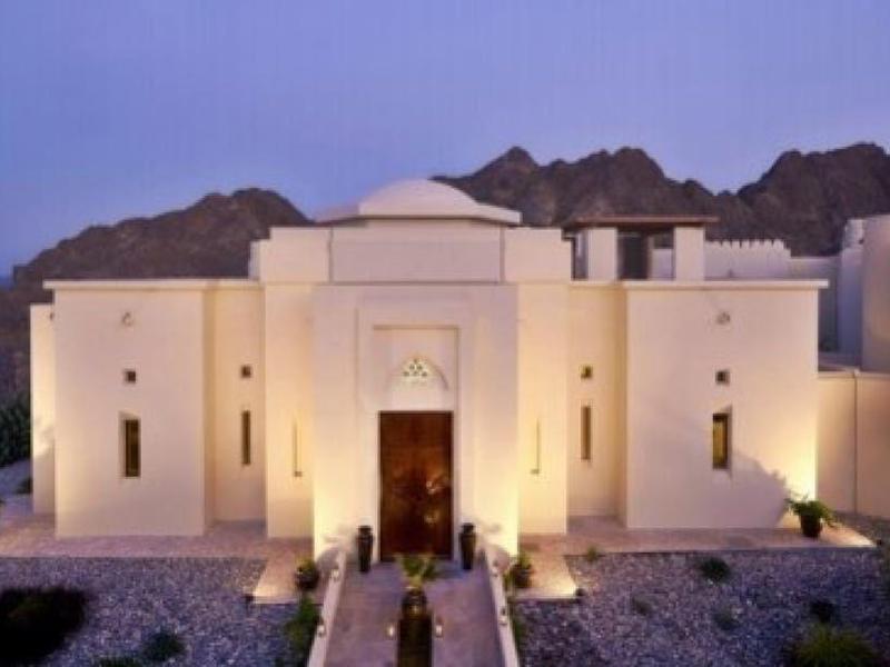 Edificio de hotel blanco junto al mar con montañas alrededor al atardecer.