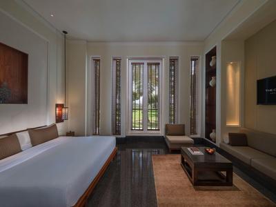 Moderní hotelový pokoj s velkou postelí, pohovkou, konferenčním stolkem a výhledem na zahradu přes balkonové dveře.