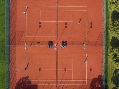 Aerial view of a red tennis court with players and surrounding greenery.