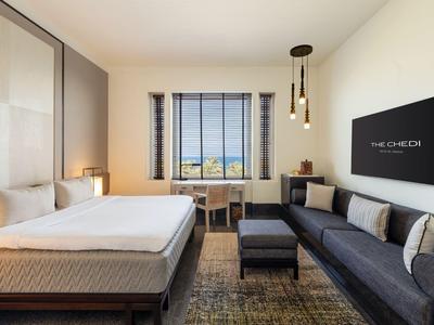 Chambre d'hôtel moderne avec grand lit, canapé, espace de travail et vue par la fenêtre.