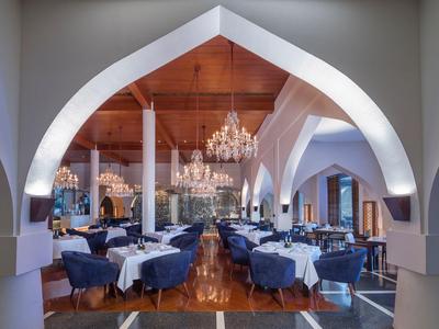 Elegant dining room with white tables, blue chairs, and chandeliers under arched ceilings.