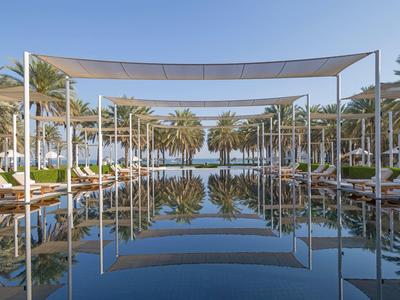 Elegantní bazénová oblast se slunečními plachtami a palmami v resortu pod jasnou oblohou.