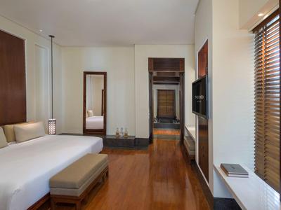 Moderní hotelový pokoj s velkou postelí, stoličkou, zrcadlem a televizí na stěně.