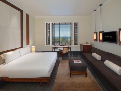 Moderní hotelový pokoj s velkou postelí, pohovkou, psacím stolem a výhledem na zeleň.