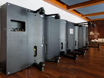 Modern gym room with several black rowing machines on wooden floor.