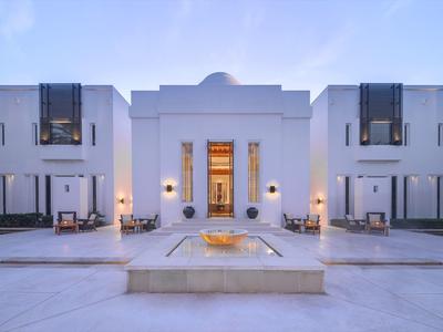 Moderní bílá budova s bazénem a posezením za soumraku.