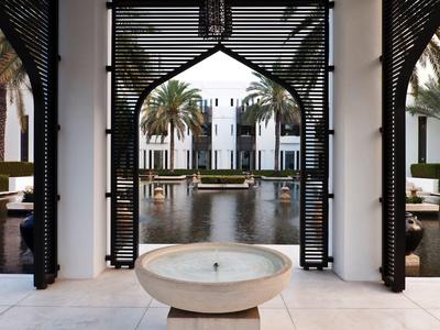 Pohled přes oblouk na vodní nádrž s palmami a bílou budovou v pozadí.