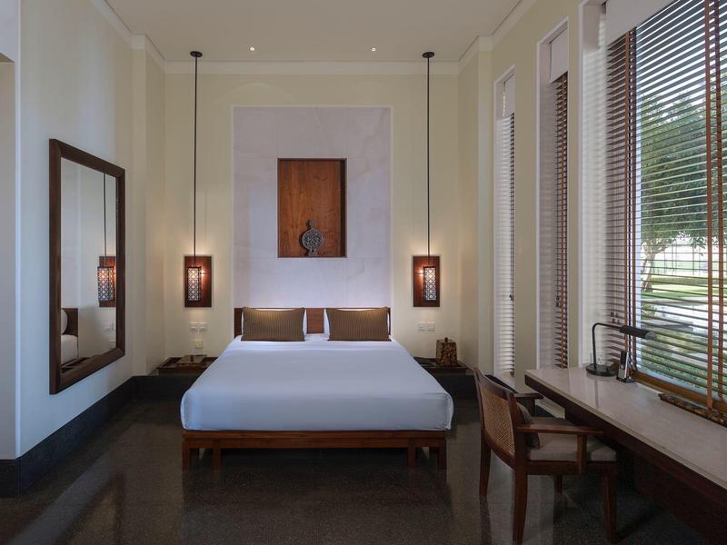 Moderní hotelový pokoj s manželskou postelí, velkým zrcadlem a stolkem u okna s žaluziemi.