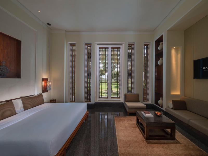 Moderní hotelový pokoj s velkou postelí, pohovkou, konferenčním stolkem a výhledem na zahradu přes balkonové dveře.