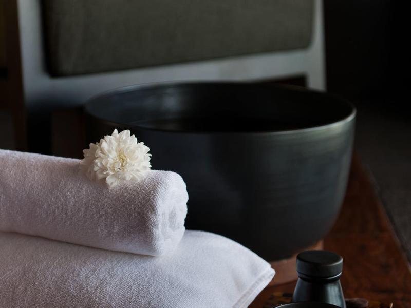 Složené bílé ručníky s lázeňskými předměty na dřevěném povrchu a rozmazané křeslo v pozadí