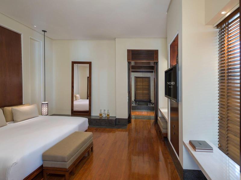 Moderní hotelový pokoj s velkou postelí, stoličkou, zrcadlem a televizí na stěně.