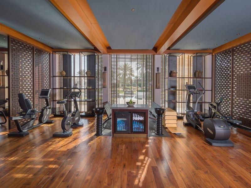 Moderní posilovna s dřevěnou podlahou, tréninkovým vybavením a velkými okny s výhledem na zahradu.