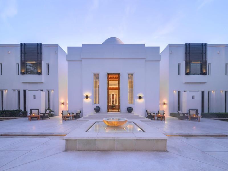 Moderní bílá budova s bazénem a posezením za soumraku.