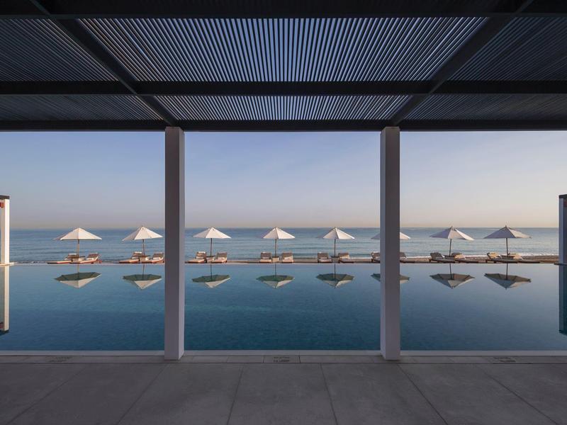 Moderní bazén s slunečníky a klidnou vodou u moře při západu slunce.