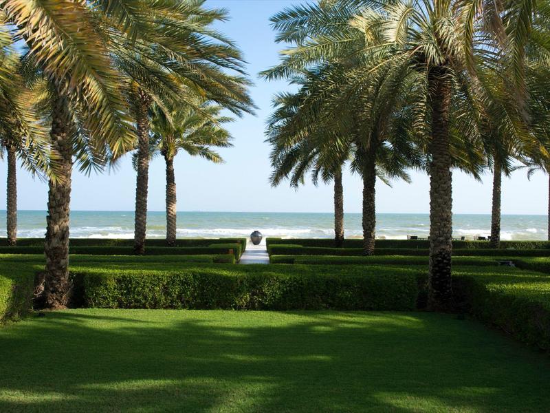 Palmy a upravená zahrada s výhledem na moře za slunečného dne.