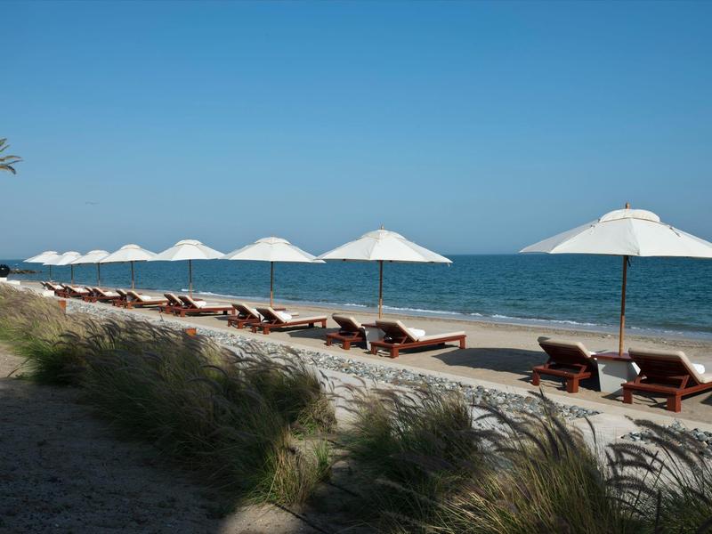 Pláž s několika bílými slunečníky a lehátky u klidného modrého moře.