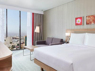 Camera d'hotel moderna con letto matrimoniale, divano, grande finestra e vista sulla città.