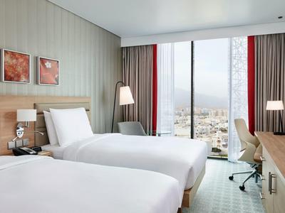 Camera d'hotel moderna con due letti singoli, grande finestra e vista sulla città.