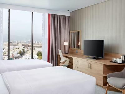 Camera d'hotel moderna con due letti e vista sulla città attraverso grandi finestre.