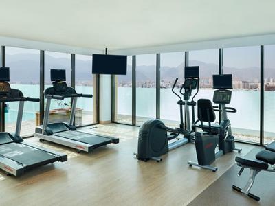 Moderner Fitnessraum mit Laufbändern, Fahrrädern und Blick auf die Stadt durch große Fenster.