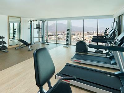 Helles Fitnessstudio mit Laufbändern, Gewichten und Panoramafenstern mit Stadtblick.