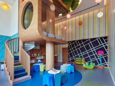 Bunter Kinderspielraum mit Holzturm, Treppe, Sitzsäcken und bunten Wanddekorationen.