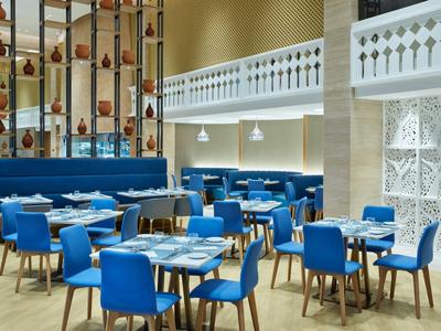 Modernes Restaurant mit blauen Stühlen, Holztischen und dekorativen Vasenregalen.