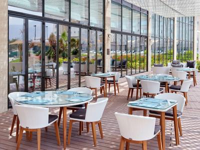 Modernes, helles Café mit Glaswänden, weißen Stühlen und runden Tischen auf Holzterrasse