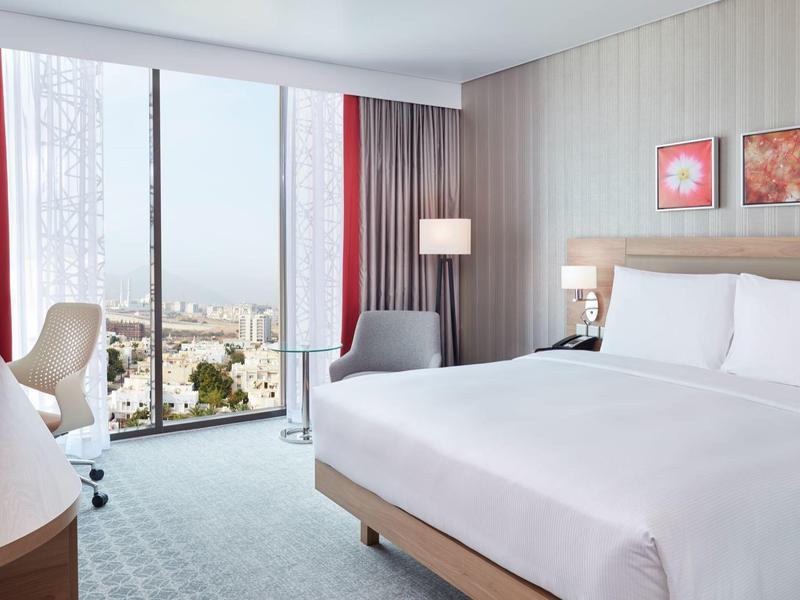 Camera d'hotel luminosa con grande finestra, letto king size, scrivania e vista sulla città.