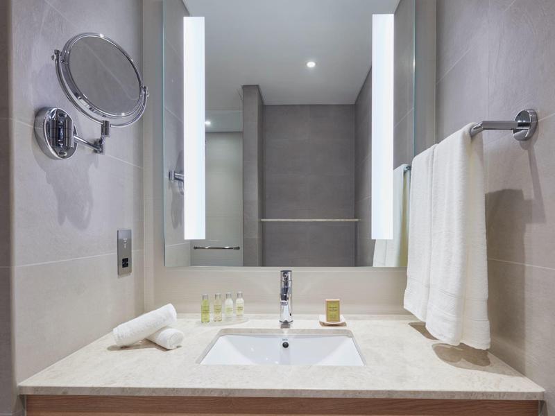 Specchio bagno moderno con illuminazione sopra il lavabo e asciugamano appeso al muro.