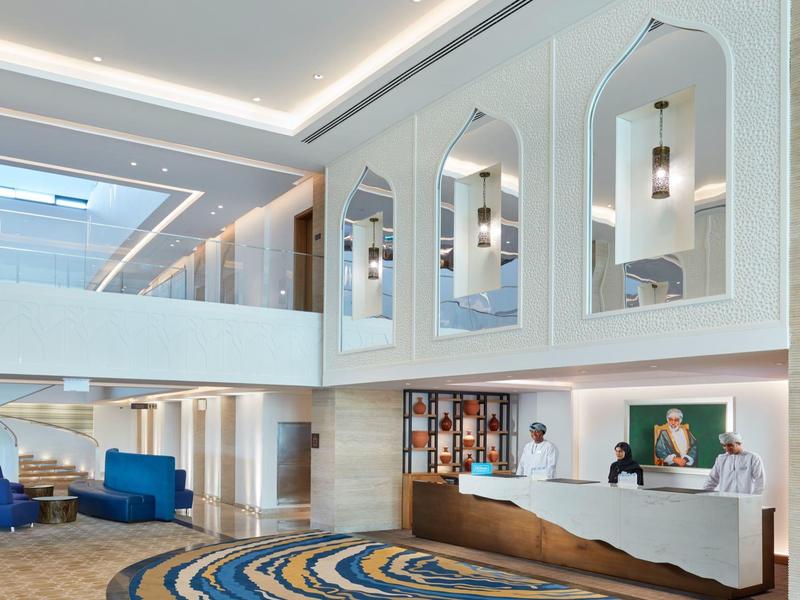 Reception di un moderno hotel con banco curvo e poltrone blu.