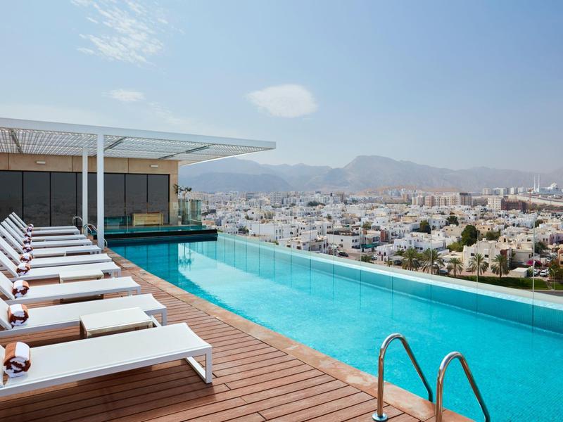 Piscina a sfioro su terrazza sul tetto con lettini e vista sulla città e le montagne.