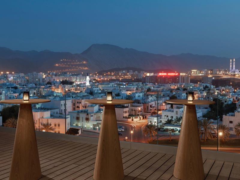 Vista da una terrazza sul tetto su una città al crepuscolo con montagne sullo sfondo.