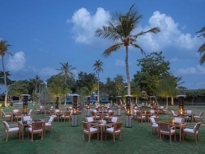 Abendveranstaltung mit gedeckten Tischen und Palmen auf einer grünen Wiese unter blauem Himmel.