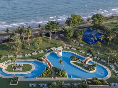 Blick auf einen Hotelpool mit Rutschen und Liegestühlen neben dem Strand.