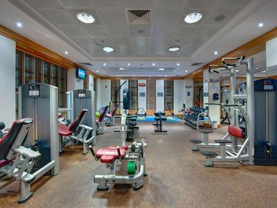 Moderner Fitnessraum mit verschiedenen Trainingsgeräten, Holzfußboden und Deckenbeleuchtung.