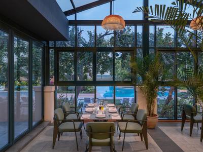 Essbereich mit Blick auf Pool und Palmen in einem Hotel mit Glaswänden und -dach.