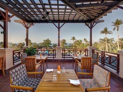 Terrasse mit Holztisch und Stühlen, Überdachung, Blick auf Palmen und klares Wetter